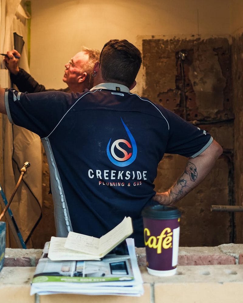 A Creekside plumber in a branded shirt marking out on a wall with a colleague